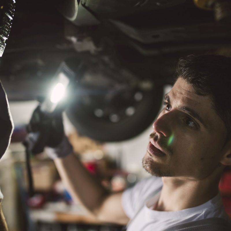 Mechanic checking the underbody of a car in a workshop Mechanic checking the underbody of a car in a workshop