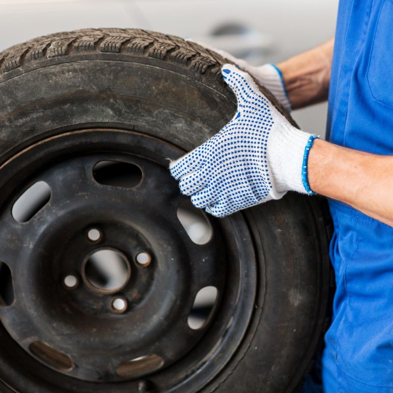 car service, repair, maintenance and people concept - auto mechanic man with wheel tire at workshop