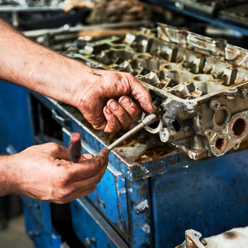 Strong worker holding instrument, equipment by dirty hands. Close up of strong worker holding instrument, equipment by dirty hands. Hardworking male wearing uniform, working in garage, workshop, servicing center. Concept of manual labor.